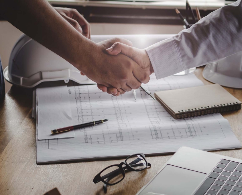 Two People Shaking Hands Over Plans